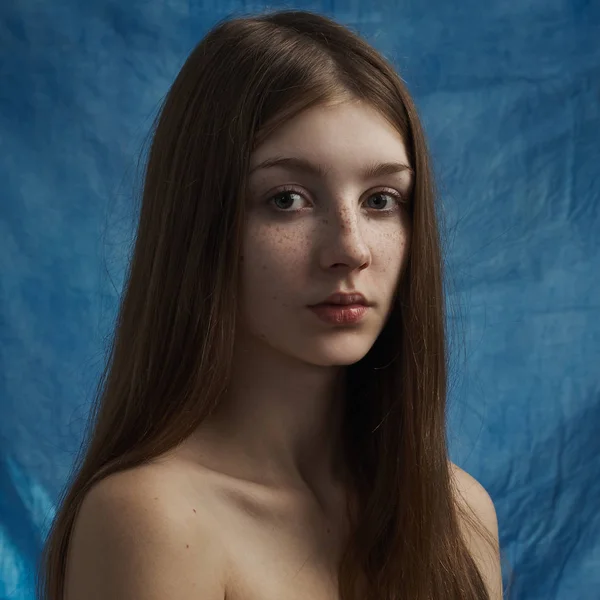 Beauty theme: portrait of a beautiful young girl with freckles on her face and wearing a black dress on a blue background in studio — Stock Photo, Image