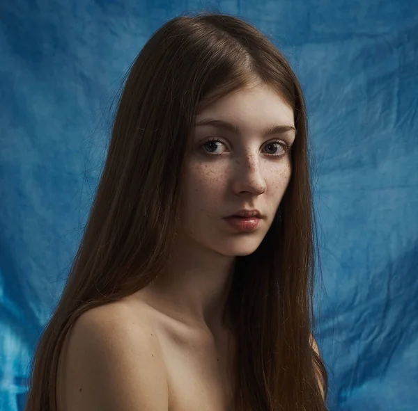 Tema kecantikan: potret seorang gadis muda yang cantik dengan bintik-bintik di wajahnya dan mengenakan gaun hitam di latar belakang biru di studio — Stok Foto