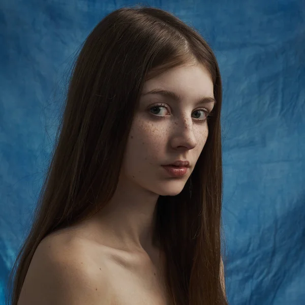 Tema da beleza: retrato de uma bela jovem com sardas em seu rosto e vestindo um vestido preto em um fundo azul em estúdio — Fotografia de Stock