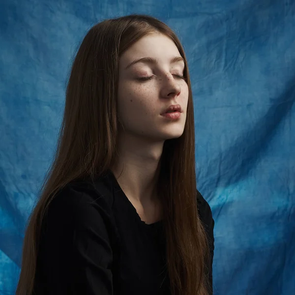 Tema de belleza: retrato de una hermosa joven con pecas en la cara y con un vestido negro sobre un fondo azul en el estudio — Foto de Stock