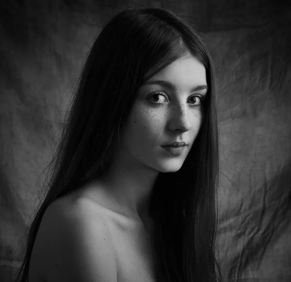 Dramatic black and white portrait of a beautiful lonely girl with freckles isolated on a dark background in studio shot — Stock Photo, Image