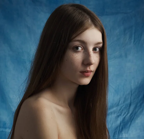 Beauty theme: portrait of a beautiful young girl with freckles on her face and wearing a black dress on a blue background in studio — Stock Photo, Image