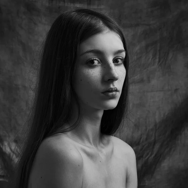Dramatic black and white portrait of a beautiful lonely girl with freckles isolated on a dark background in studio shot — Stock Photo, Image