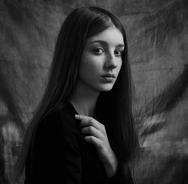 Dramatic black and white portrait of a beautiful lonely girl with freckles isolated on a dark background in studio shot — Stock Photo, Image