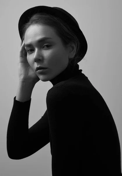 Dramatic black and white portrait of young beautiful girl with freckles in a black turtleneck and a hat on a white background in studio