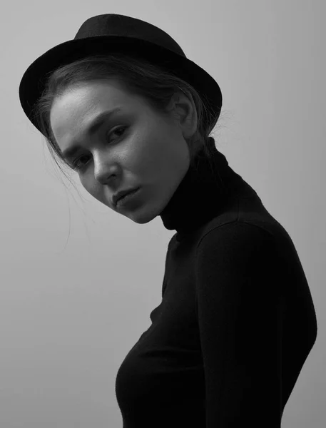 Dramatic black and white portrait of young beautiful girl with freckles in a black turtleneck and a hat on a white background in studio