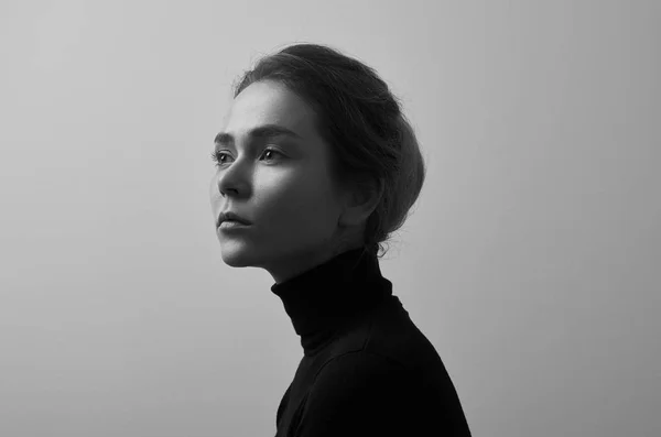 Dramatic black and white portrait of young beautiful girl with freckles in a black turtleneck on white background in studio — Stock Photo, Image