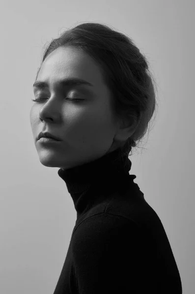 Dramatic black and white portrait of young beautiful girl with freckles in a black turtleneck on white background in studio — Stock Photo, Image