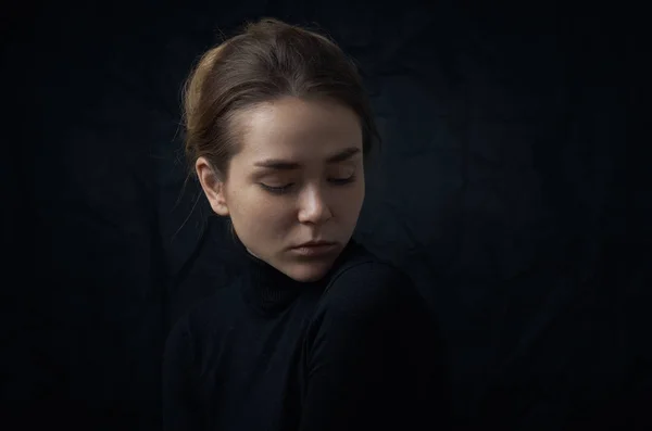 Dramatic portrait of a young beautiful girl with freckles in a black turtleneck on black background in studio — Stock Photo, Image