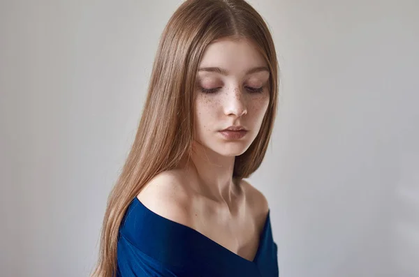 Tema de belleza: retrato de una hermosa joven con pecas en la cara y con un vestido azul sobre un fondo blanco en el estudio — Foto de Stock