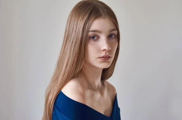 Tema de belleza: retrato de una hermosa joven con pecas en la cara y con un vestido azul sobre un fondo blanco en el estudio —  Fotos de Stock