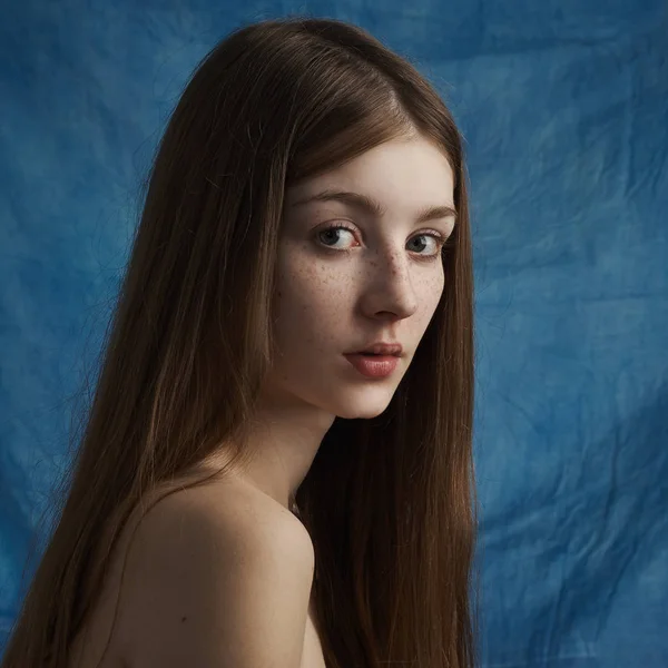 Skönhet tema: porträtt av en vacker ung flicka med fräknar på hennes ansikte och bär en svart klänning på en blå bakgrund i studio Royaltyfria Stockbilder