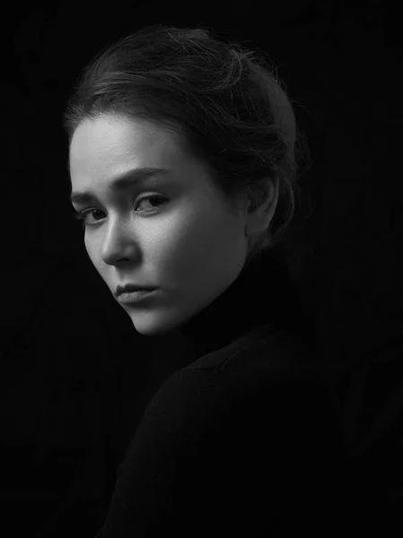 Dramatiska svartvita porträtt av ung vacker flicka med fräknar i en svart polotröja på svart bakgrund i studio Stockbild