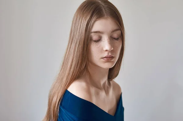 美主题︰ 一个美丽的年轻女孩，在她的脸，穿着一件蓝色连衣裙在工作室中的白色背景上的雀斑的肖像 — 图库照片