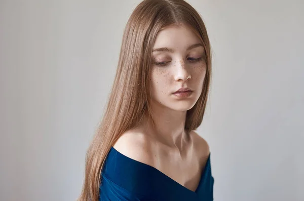 Skönhet tema: porträtt av en vacker ung flicka med fräknar på hennes ansikte och klädd i en blå klänning på en vit bakgrund i studio — Stockfoto