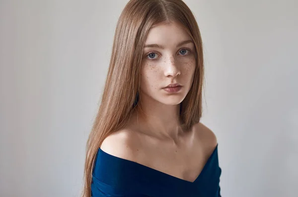 Schoonheid thema: portret van een mooi jong meisje met sproeten op haar gezicht en draagt een blauwe jurk op een witte achtergrond in de studio — Stockfoto
