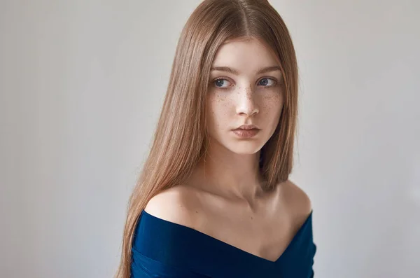 Skönhet tema: porträtt av en vacker ung flicka med fräknar på hennes ansikte och klädd i en blå klänning på en vit bakgrund i studio — Stockfoto