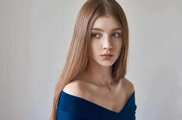 Beauty theme: portrait of a beautiful young girl with freckles on her face and wearing a blue dress on a white background in studio — Stock Photo, Image