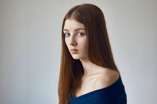 Тема красоты: портрет красивой молодой девушки с веснушками на лице и в синем платье на белом фоне в студии — стоковое фото