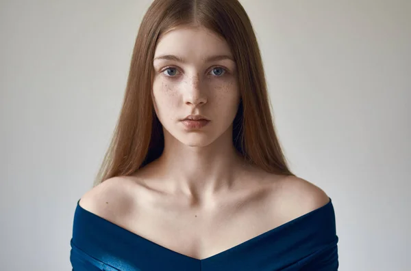 Тема красоты: портрет красивой молодой девушки с веснушками на лице и в синем платье на белом фоне в студии — стоковое фото