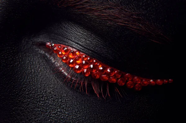 Μακροεντολή και close-up δημιουργικό μακιγιάζ θέμα: όμορφα θηλυκά μάτια με μαύρο δέρμα και κόκκινα διαμάντια, retouched φωτογραφία — Φωτογραφία Αρχείου