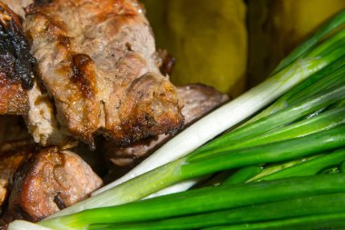 Izgara et, barbekü, taze yeşil soğan ve tuzlanmış salatalıkla birlikte beyaz bir tabakta. Ahşap masa arkasında