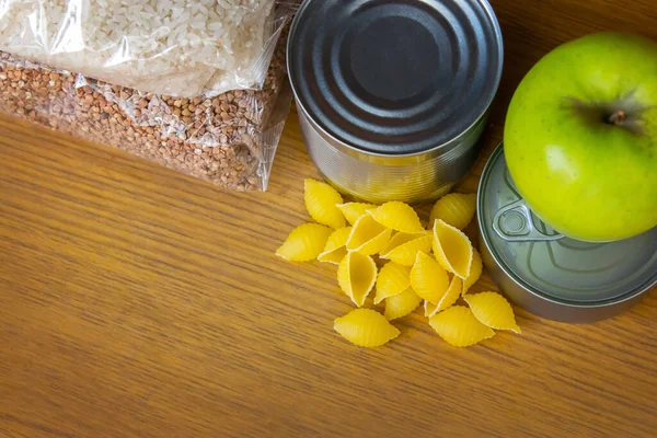 Tin can, canned food, pasta, buckwheat and rice on a wooden background. Food delivery. Food donation. delivers food. Brick wall backdrop. Blank space for text insertion