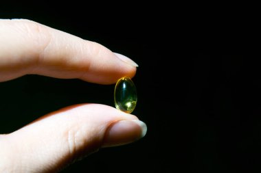 Elinde sarı şeffaf tablet. Lumene kadar şeffaf. Virüs için kaliteli ilaç. Siyah arka planda vitaminler. Eklenecek yer