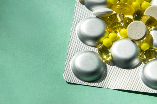 Çeşitli şekil ve renklerde dağıtım hapları, şeffaf sarı, büyük beyaz. Bir sürü hap. Yeşil-mavi arka planda. Vitaminler virüsle savaşır. Eklenecek yer.