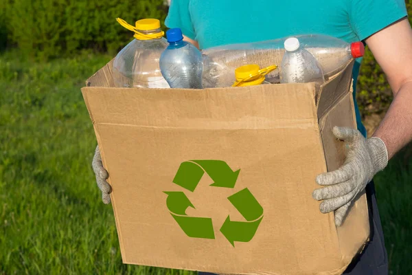 ボランティアがゴミを片付けます プラスチックボトルの箱を手に手袋をしている男 生態学 純粋な自然 分別収集 プラスチックは止めて リサイクル 廃棄物ゼロ — ストック写真