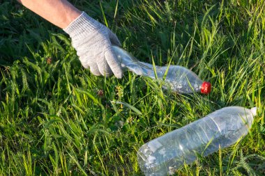 Çöpü temizleyen gönüllü. Eldivenli bir el, açıklıktan plastik şişeleri temizler. Ekoloji. Saf doğa. Ayrı çöp toplama yeri. Plastiği durdur. Geri dönüşüm. Sıfır atık.