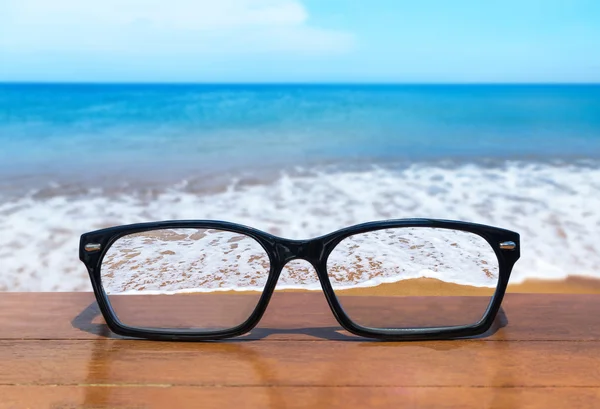 Óculos na mesa de madeira em frente ao mar tropical — Fotografia de Stock