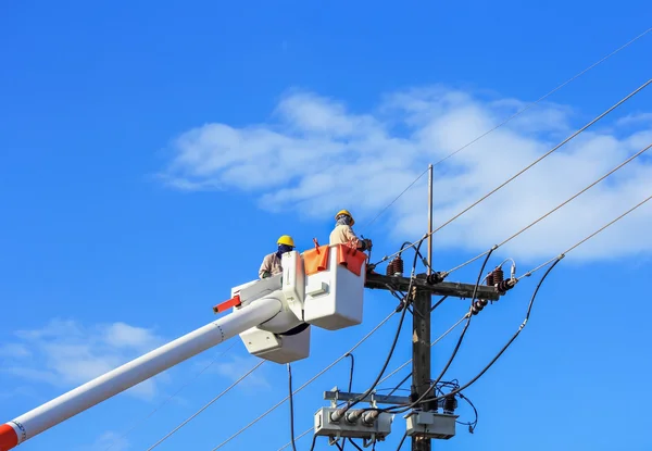 Técnicos trabajan reparando el cable de la línea de energía en un cubo en lo alto del poste de energía — Foto de Stock