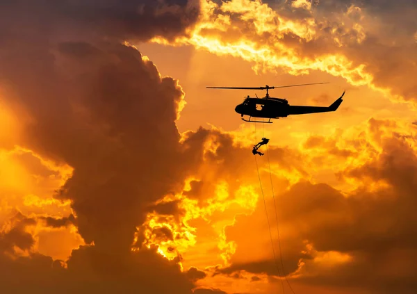 Silhouette soldiers in action rappelling climb down from helicopter on sunset background — Stock Photo, Image
