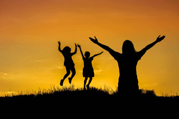 Silhouette mother standing raised hands up with children jumping to sky on sunset happy time family concept