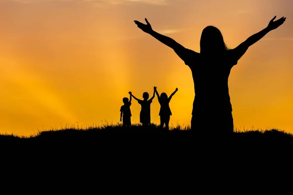 Silhouette mother and children standing raised hands up on sunset — Stock Photo, Image