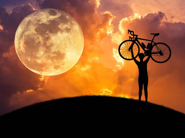 Silhouette des Mannes, der bei Sonnenuntergang mit Vollmondhintergrund ein Fahrrad über seinen Kopf hebt. — Stockfoto