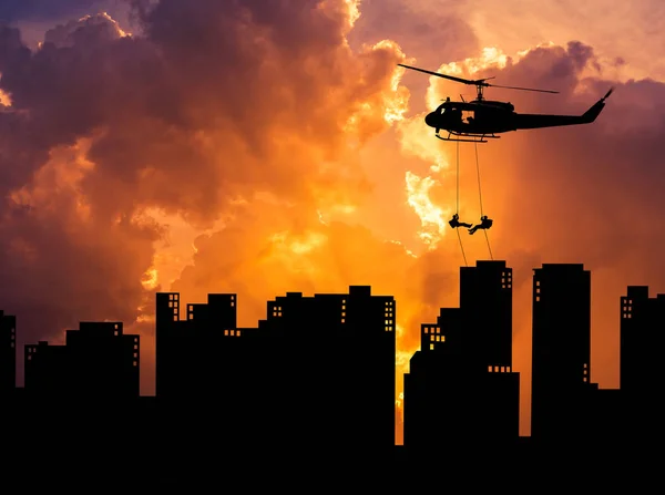 Soldados silhueta em ação rapel descer de helicóptero na construção de arranha-céus ao pôr-do-sol — Fotografia de Stock