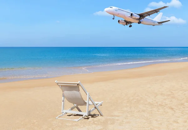 Avião de passageiros branco pousando acima do mar azul com cadeira de praia de madeira branca na praia tropical — Fotografia de Stock