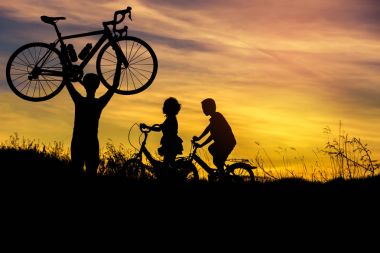 Küçük çocuk ve küçük kız eğleniyor başının üzerinde bisiklet kaldırma adam siluet günbatımı motora binme  