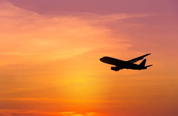 Avión de pasajeros de silueta volando hacia el cielo a gran altitud durante la puesta del sol — Foto de Stock