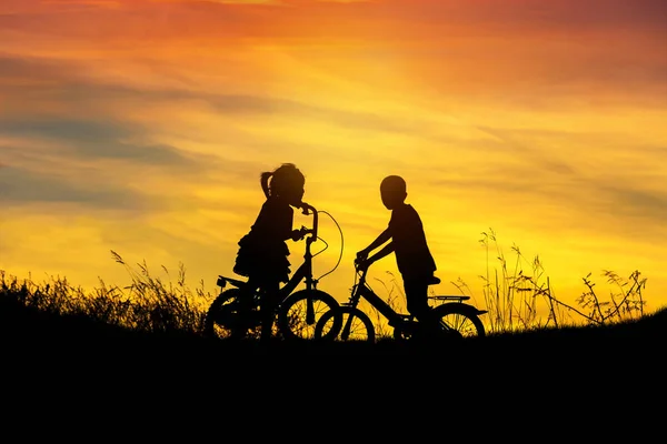 Silhueta menino e menina se divertindo andar de bicicleta no por do sol — Fotografia de Stock