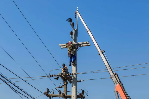 Electricistas escalando trabajos en poste de energía eléctrica con grúa — Foto de Stock