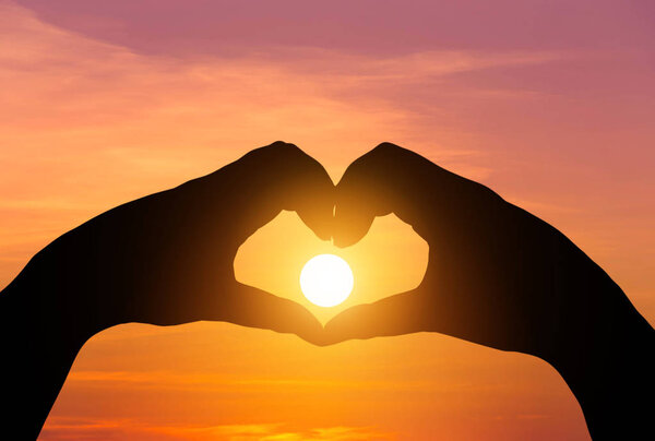 Silhouette two hands making form heart shape with sun sunset
