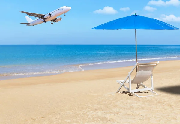 Avião de passageiros que voa pousando acima da praia tropical com cadeira de praia de madeira branca e guarda-sol azul — Fotografia de Stock