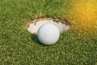 Yeşil çimenlerin üzerinde delik yakınındaki beyaz golf topu