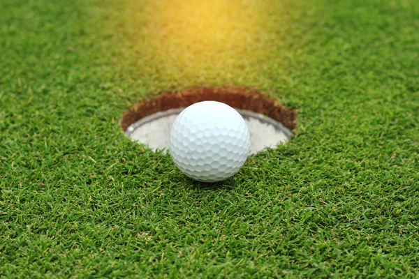 Закрыть белый мяч для гольфа возле лунки на зеленой траве — стоковое фото