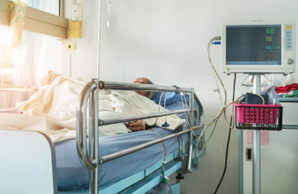 Cama de la sala de hospitalización durante el sueño del paciente de edad avanzada con dispositivo digital para medir el monitor de presión arterial —  Fotos de Stock