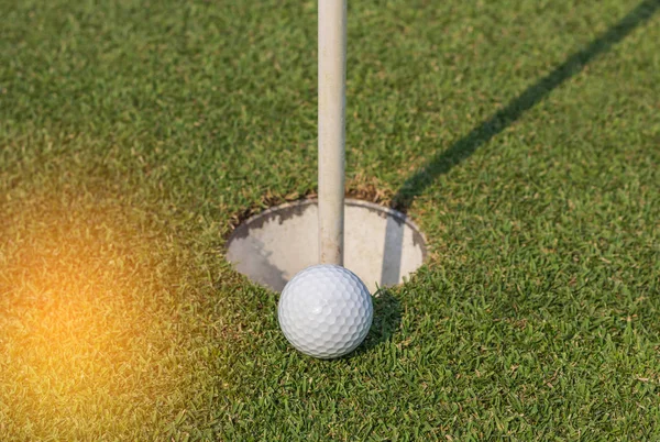 Bola de golfe branco perto do buraco na grama verde — Fotografia de Stock