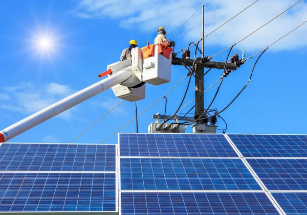 Electricians repairing wire of the power line on bucket hydraulic lifting platform with photovoltaics in solar power station